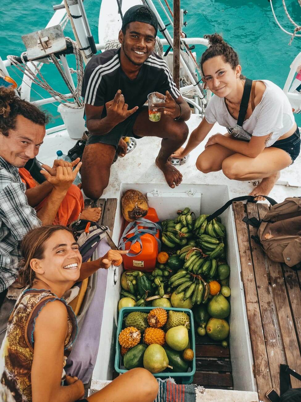 Un groupe de jeunes prenant la pose devant le cockpit d&rsquo;un voilier remplis de fruits