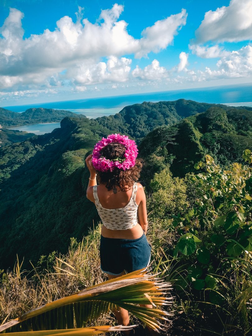 Une jeune femme coiffée d&rsquo;une couronne de fleurs roses vue de dos devant un panorama