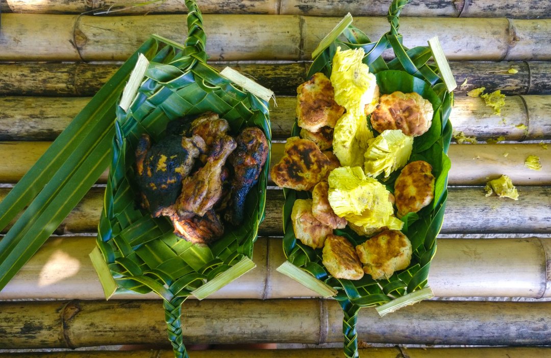 Des cuisses de poulet grillé, du pain coco et de la chair de uru dans des plats de feuilles de cocotier tressées