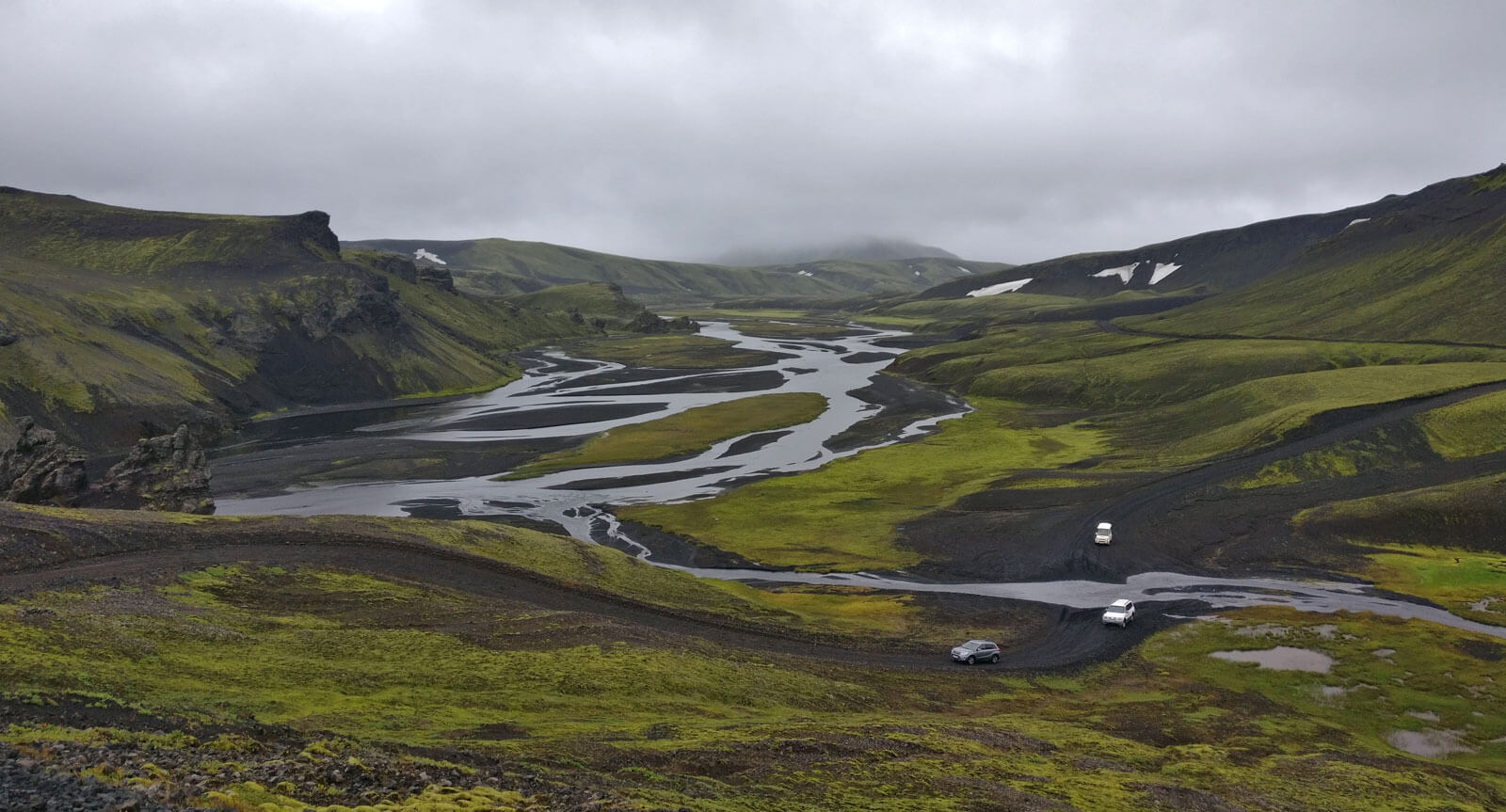 Un paysage de terre volcanique noire et de mousse verte traversé par une rivière