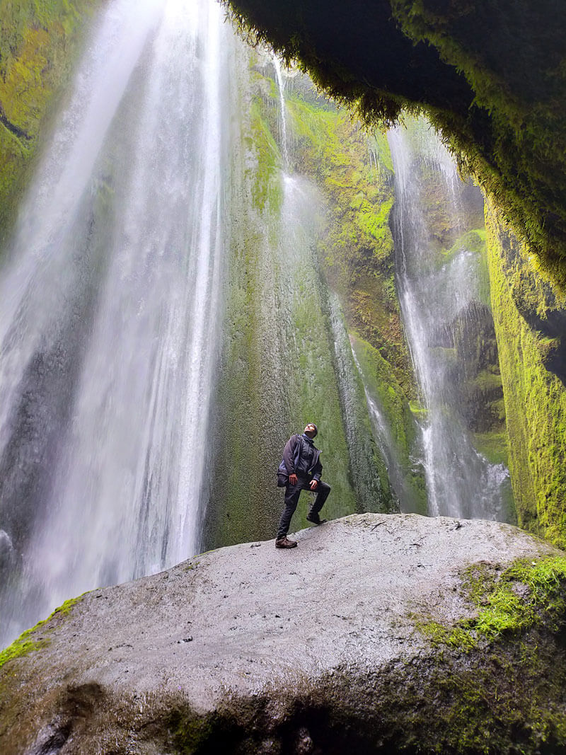 Une cascade dans une caverne avec un homme au centre debout sur un rocher et regardant vers le haut