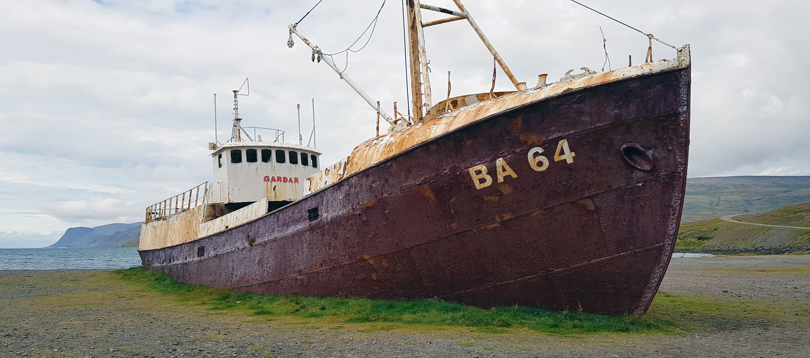 Vieux navire métallique posé sur la berge avec l&rsquo;inscription &ldquo;BA 64&rdquo; sur la coque