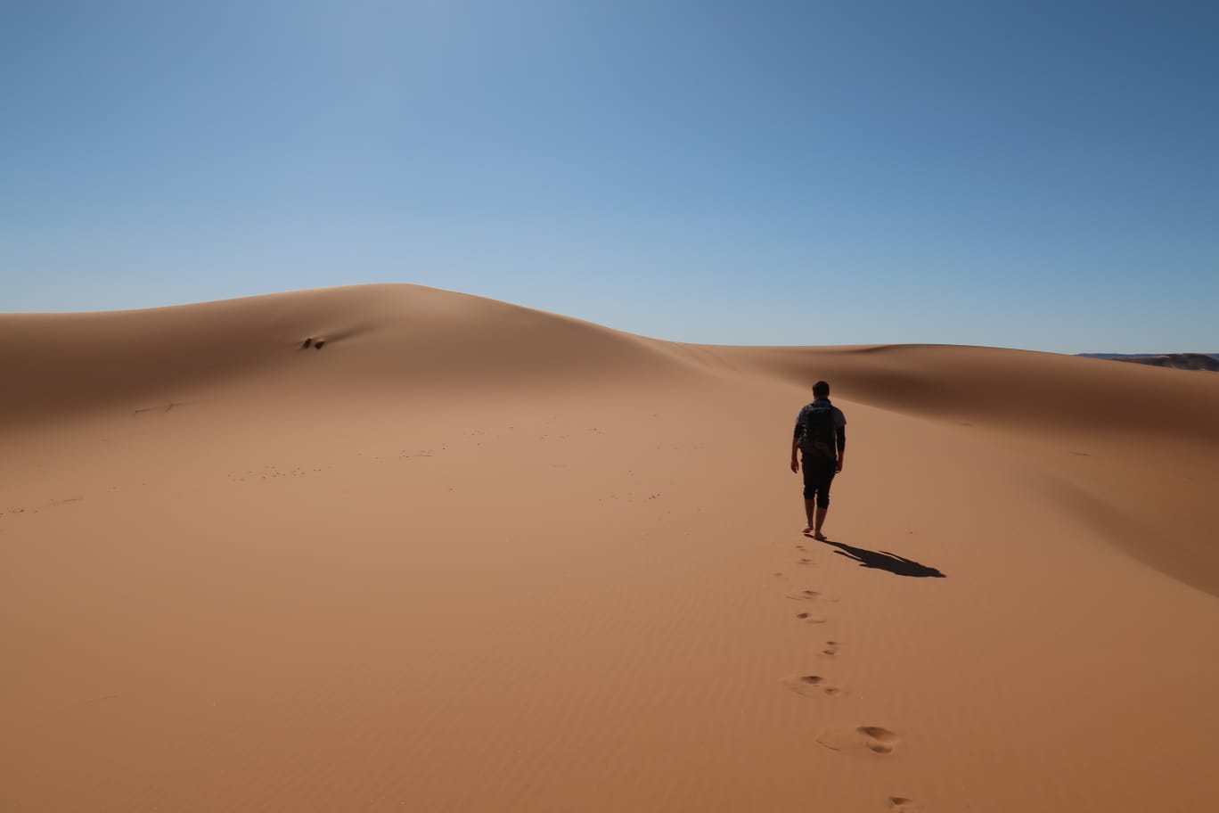 Une silhouette d'un homme avec un sac à dos, gravissant une dune de sable vue de dos