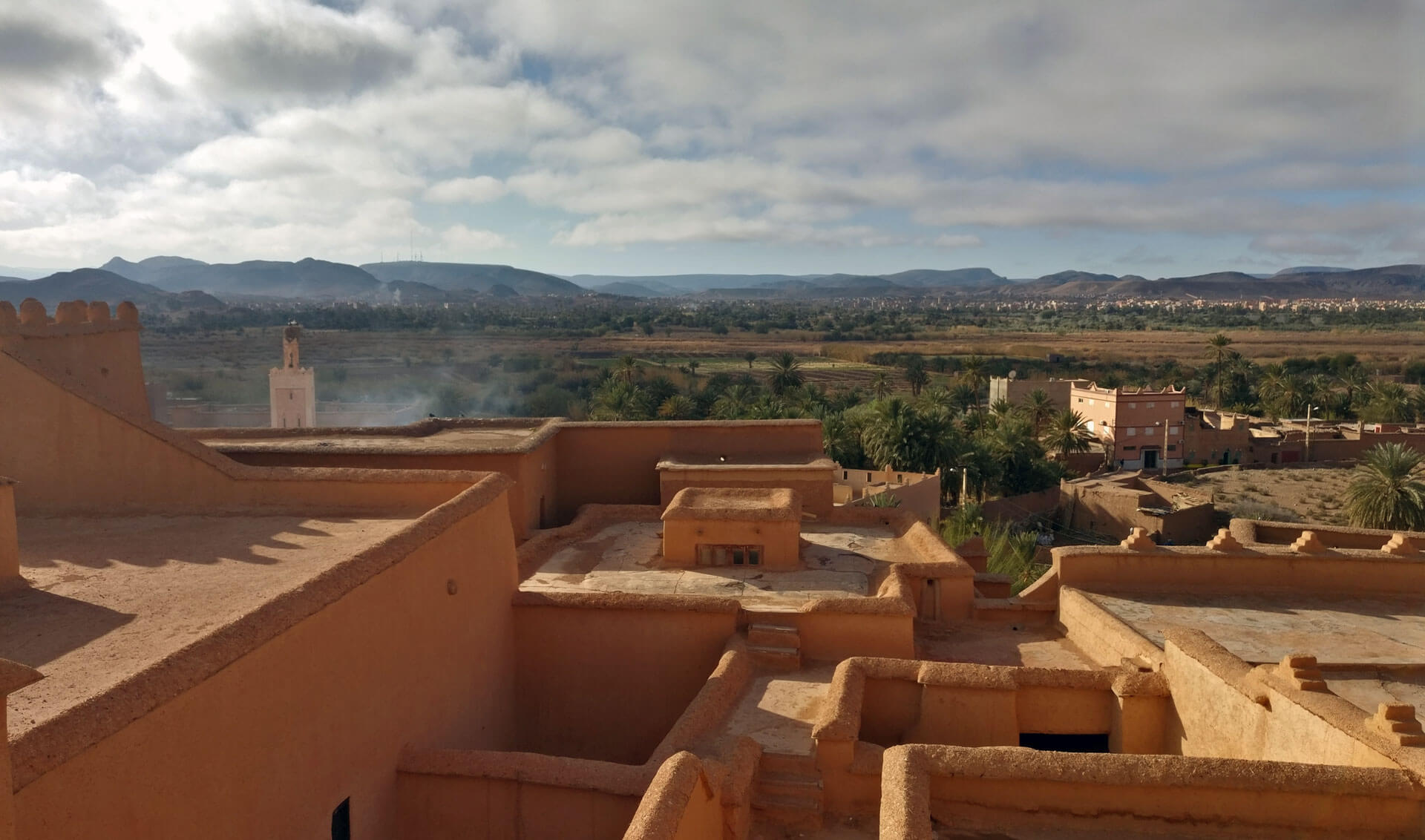 Quelques toits plats en terre de la petite ville de Ouarzazate, avec les palmiers et montagnes qui s&rsquo;étendent à l&rsquo;horizon.