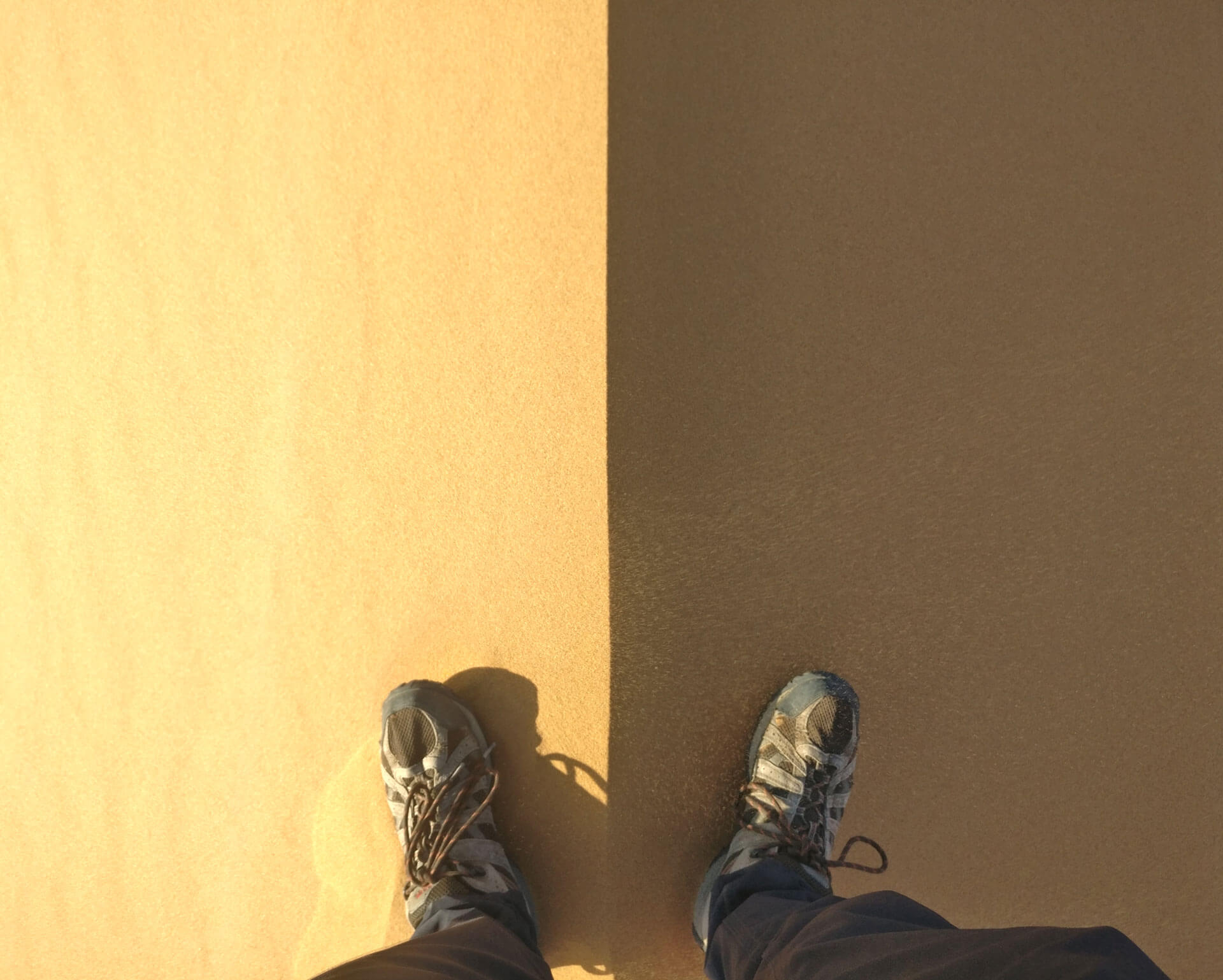 Une photo de pieds de part et d&rsquo;autre de l&rsquo;arrête d&rsquo;une dune, le côté droit à l&rsquo;ombre, et le gauche au soleil