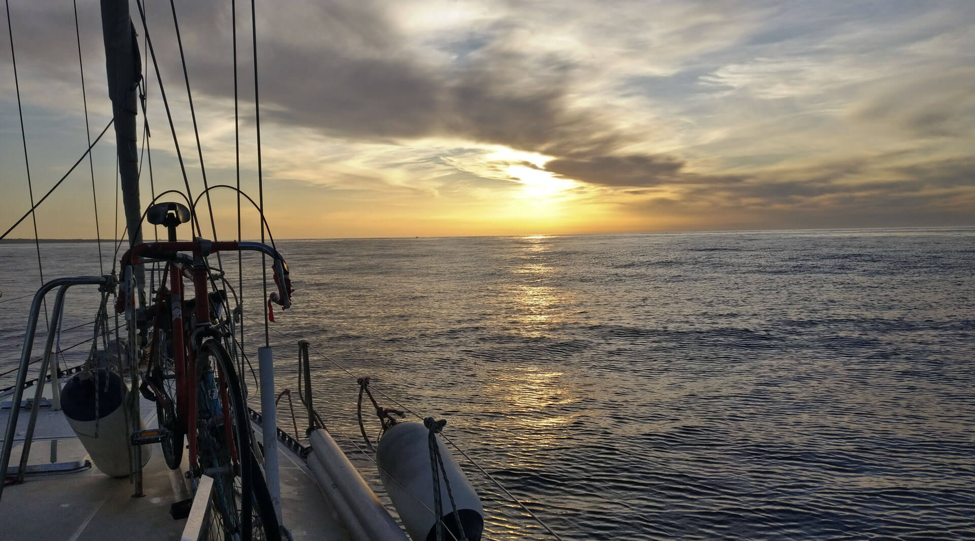 Le soleil se couche sur l&rsquo;horizon, vu depuis le pont d&rsquo;un bateau sur lequel des vélos sont attachés